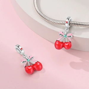 Macro detail of silver cherry charm with red enamel and pink bow on snake chain