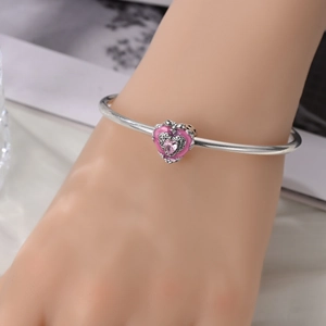 Detail of a silver open bangle with a pink enamel heart charm and gemstone inlay
