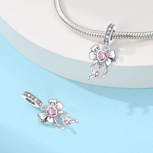 Macro detail of a silver bow charm with pink heart zirconia on a snake chain bracelet