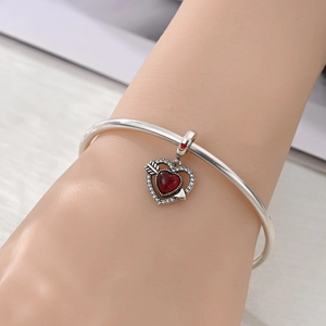 Nahaufnahme des herzförmigen Flügelanhängers mit rotem Edelstein am Silberarmband