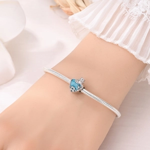 Gros plan sur breloque coeur bleu et bracelet chaîne serpent en argent avec dentelle