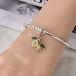 Close-up of a silver sunflower charm with yellow petals and green zircon leaves on a bracelet