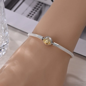 Close-up of silver mesh bracelet featuring a gold crown charm with white crystals