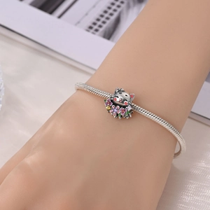 Gros plan d'un bracelet maille serpent en argent avec un pendentif chat et fleurs colorées