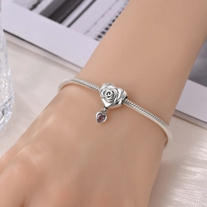 Detail of silver snake chain bracelet featuring a rose heart charm and pink heart pendant