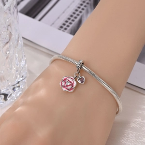Wrist view of a silver snake chain bracelet with pink rose and purple heart charms
