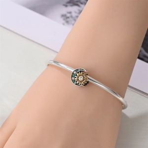 Silver bangle with gold sunflower and crescent moon charm set with green gemstones