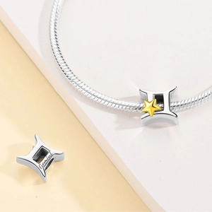 Close-up of Gemini zodiac charm with gold star detail on a silver snake chain bracelet