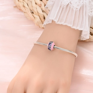 Detailed view of a silver charm bracelet with pink enamel and purple zircon on a model