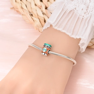 Detail eines silbernen Schlangenarmbands mit buntem Kaffeetassen-Emaille-Charm am Handgelenk