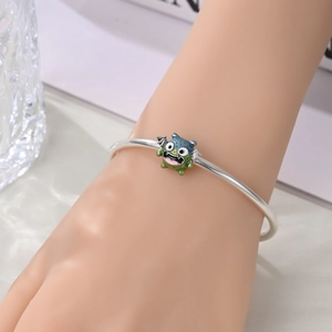 Detail of silver bracelet with colorful cartoon monster charm on a female wrist