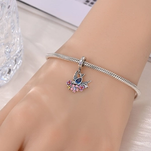 Detail of silver snake chain bracelet with bird and flower pendant in garden style