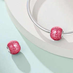 Dettaglio di charms floreali in smalto rosa con motivi a rose su un bracciale argento