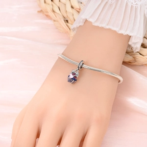 Close-up of a silver cupcake charm bracelet with pink and blue gems on a satin background