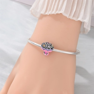Macro shot of a floral bouquet charm with pink enamel and colorful zircons on a silver bangle