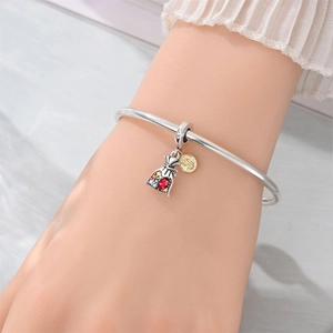 Silver bangle with multi-colored gemstone money bag and gold coin charm on wrist