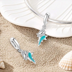Detail of silver conch shell charm with blue enamel and sparkling zircon on a beach