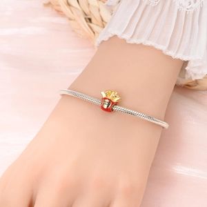 Detail of silver snake chain bracelet with red and gold french fries charm on wrist