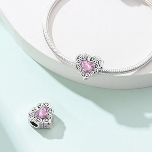 Detail van zilveren hartbedel met roze zirkoon en filigraanpatroon aan armband