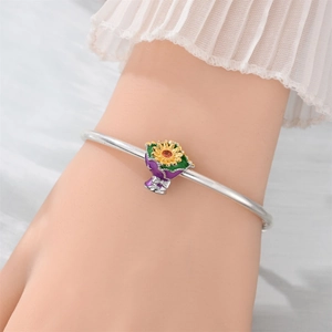 Detail of silver bangle featuring a colorful enamel sunflower charm and floral pendant