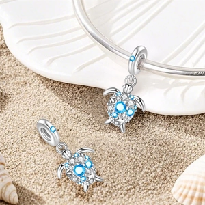 Detailed view of silver sea turtle charms with blue zircon stones on sandy beach