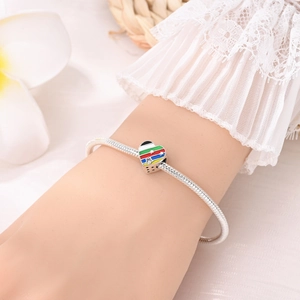 Primer plano de un dije de corazón con rayas de colores en una pulsera de cadena plana