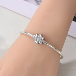 Detail of silver-plated open bangle with crystal lotus flower charm on female wrist