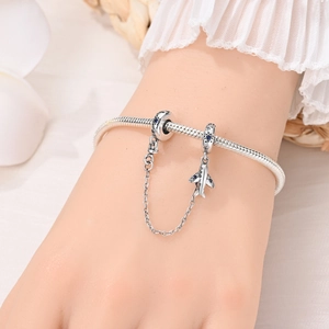Dettaglio macro di un bracciale argento con perle di zircone blu e ciondolo aereo