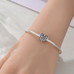 Detail of silver heart charm with pink purple gemstone and spiral texture on bracelet