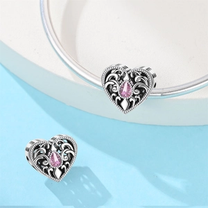 Macro shot of silver heart charm with pink gemstone and vintage vine pattern detail