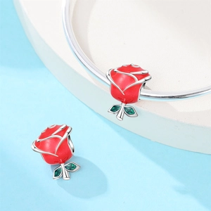 Detail of red enamel rose charm with green stones on silver snake chain bracelet