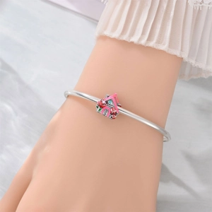 Detail of silver bracelet featuring a pink and red enamel house charm worn on a wrist
