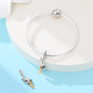 Close-up of silver bangle featuring a prayer hands charm with a gold dollar sign detail