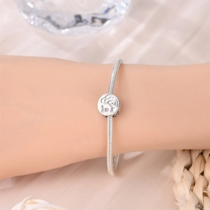 Detalle de una pulsera de dijes plateada con un colgante de corazón Mom Me en una modelo