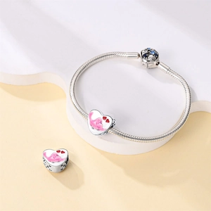 Detalle de pulsera de cadena de serpiente plateada con dijes de pájaro rosa corazón y circón