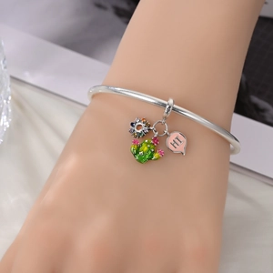 Detail of silver bangle featuring colorful enamel cactus and heart-shaped pendant