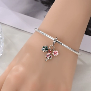 Silver bangle with pink flamingo, monstera leaf and floral enamel charms on wrist