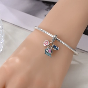 Detail of silver bangle with enamel pink flower, blue teapot and butterfly charms on wrist