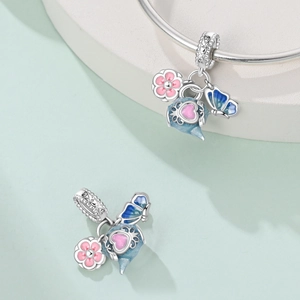 Detailed macro view of pink enamel flower and blue teapot charms on a silver bracelet