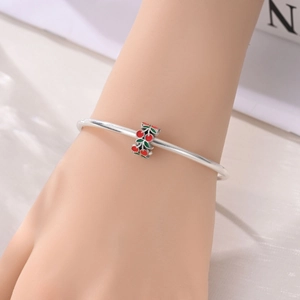 Nahaufnahme eines versilberten Armbands mit roten Kirschen-Emaille-Anhängern und grünen Blättern