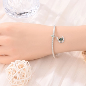 Close-up of silver horseshoe charm with green clover and LUCK engraving on snake chain