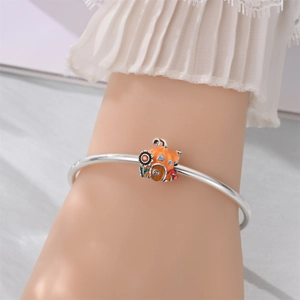 Detailed view of an orange pumpkin house enamel charm on a silver bangle bracelet