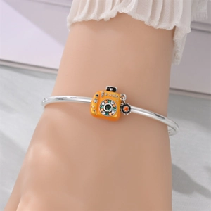 Detailed shot of a silver charm bracelet with an orange retro camera and sun pendant