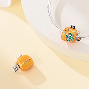 Macro detail of enamel camera charm with Hello engraving and daisy flower pendant