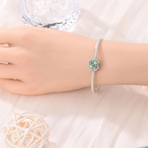 Detailed view of a silver snake chain bracelet with green clover charm on a wrist