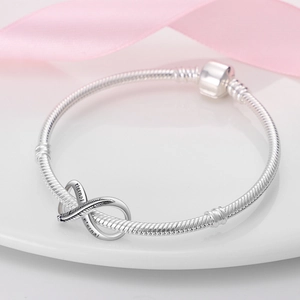 Macro view of silver snake chain bracelet featuring engraved eternal infinity charm detail