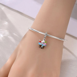 Primer plano de una pulsera plateada con un dije de cupcake de esmalte colorido en la muñeca