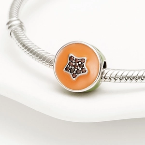 Primer plano de charm de estrella naranja con gemas marrones en pulsera de serpiente