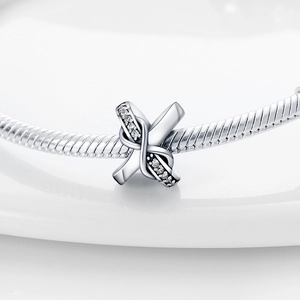 Vue macro d'un charm en forme de X argenté avec zircons sur un bracelet serpent