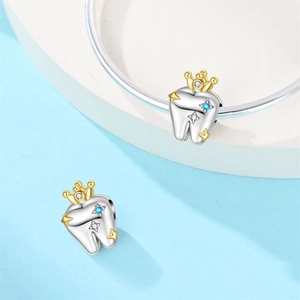 Detailed view of silver tooth charms with gold crowns and blue zircon on a bracelet
